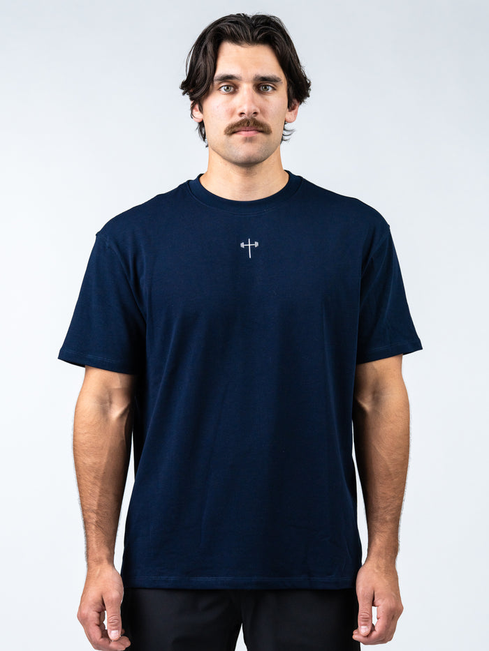 Man wearing a navy blue t-shirt with a small logo on a white background