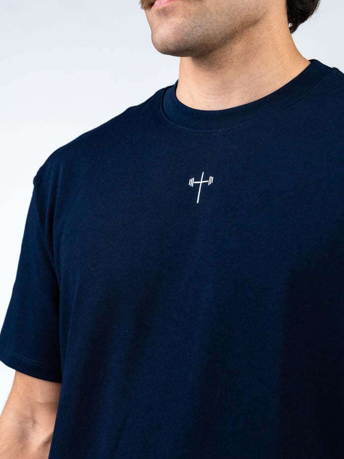 Close-up of a man wearing a navy blue Archangel Michael Premium Oversized Tee featuring a small white cross with barbell design at the center front, blending Christian fitness apparel and faith-based workout style.