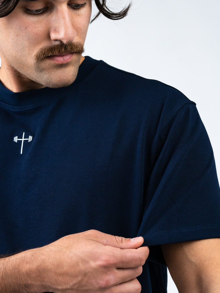 Man wearing a navy blue Archangel Michael Premium Oversized Tee featuring a small white barbell cross design near the collar, highlighting Christian gym clothing.