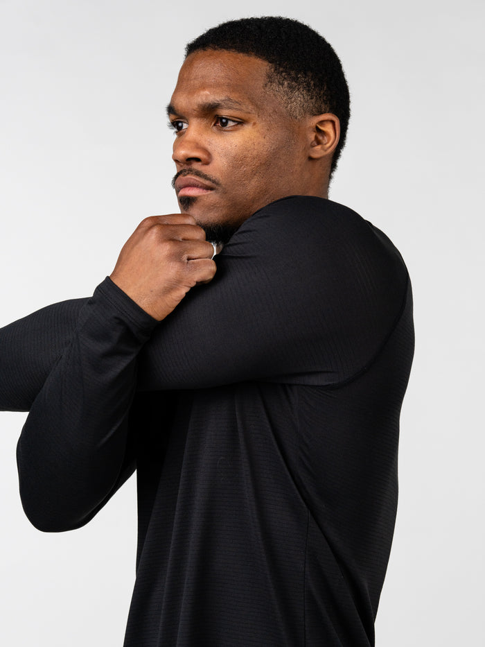 Man wearing a black Carry Your Cross Premium Long Sleeve Tee stretching his arms, demonstrating comfortable fit and flexible Christian fitness apparel.