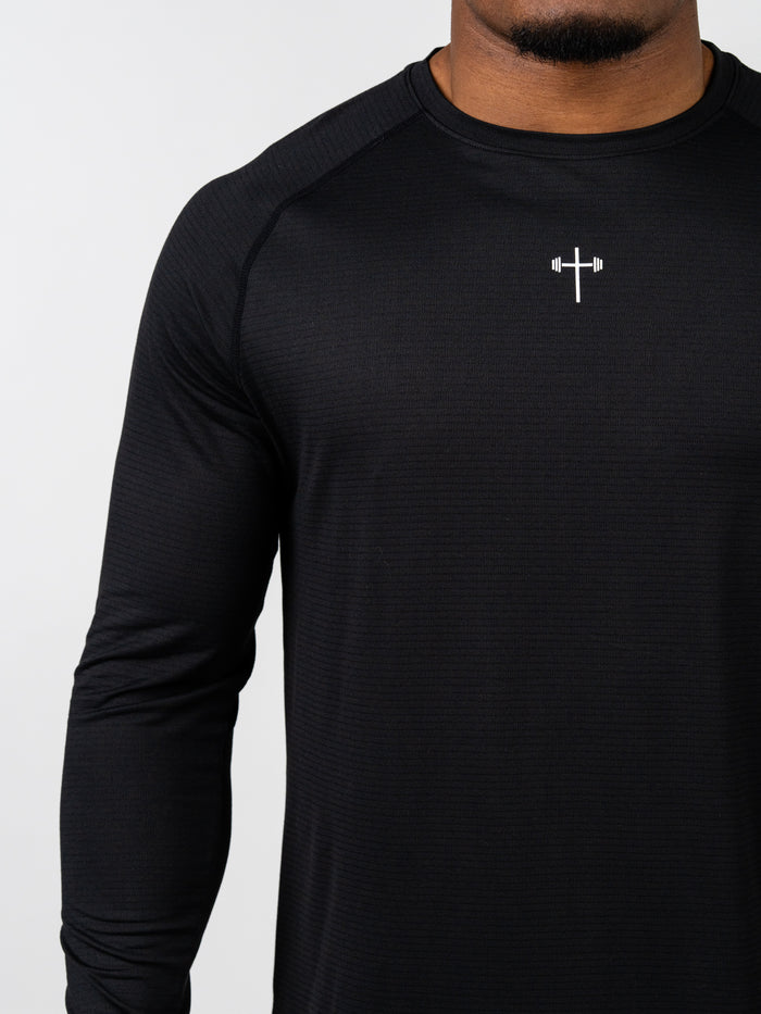 Close-up of a man wearing a black Carry Your Cross Premium Long Sleeve Tee featuring a small white cross with a barbell design on the chest, representing Christian fitness apparel.