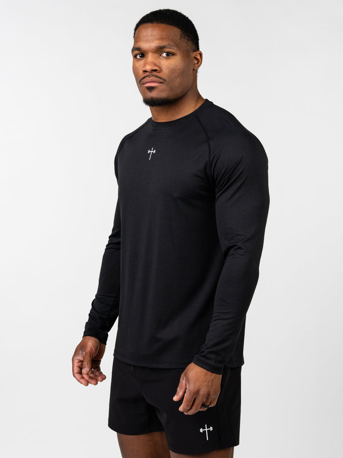 Man wearing a black Carry Your Cross Premium Long Sleeve Tee with a small cross and barbell design on the chest, paired with matching black shorts featuring the same logo.