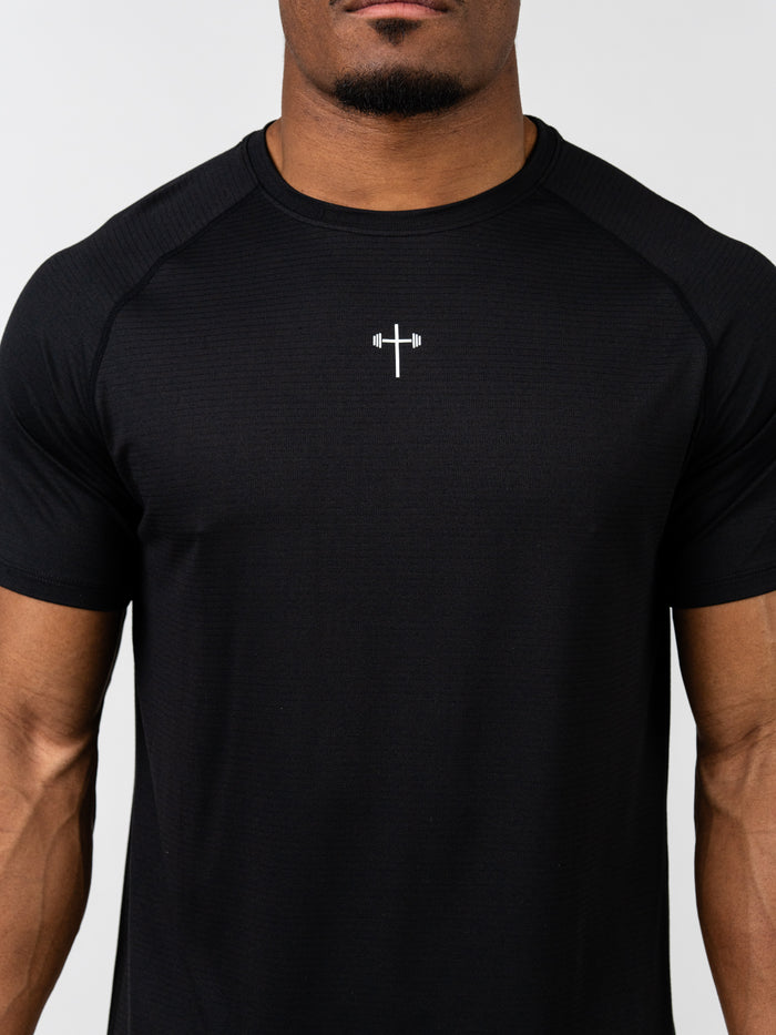 Man wearing a black Carry Your Cross Premium Tee with a small white cross and barbell graphic centered on the chest, representing Christian gym clothing.