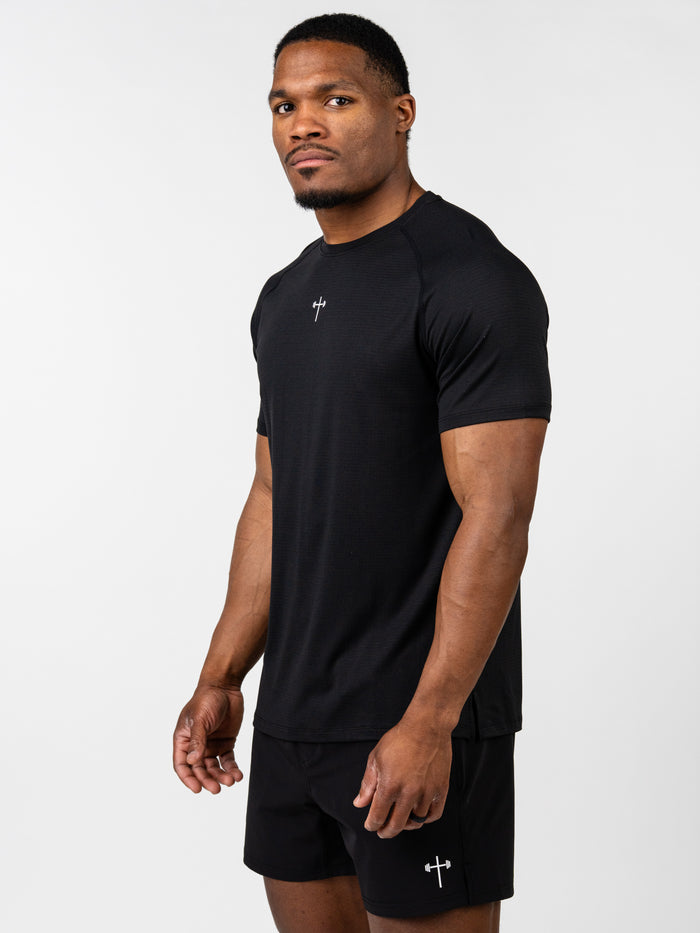Athletic man wearing a black Carry Your Cross Premium Tee with a small cross and barbell logo on the chest, styled with matching black shorts, showcasing Christian fitness apparel.