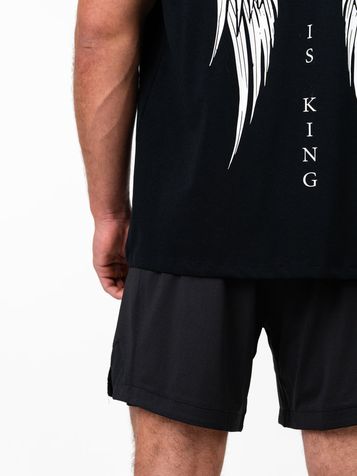 Back view of a person wearing the black Christ is King Wing Premium Oversized Tee with white wing and cross graphics, paired with black athletic shorts.