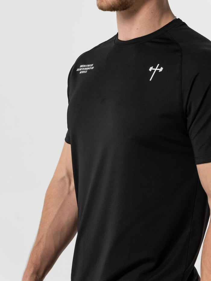 Male model wearing a black Christian Lifting Club Premium Fitted Tee featuring a small white barbell cross logo on the chest, showcasing faith-based Christian gym clothing.