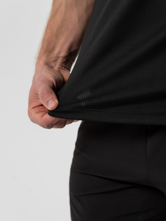 Close-up of a person wearing a black Christian Lifting Club Premium Fitted Tee, showing the lightweight fabric and small perforated detail near the hem.