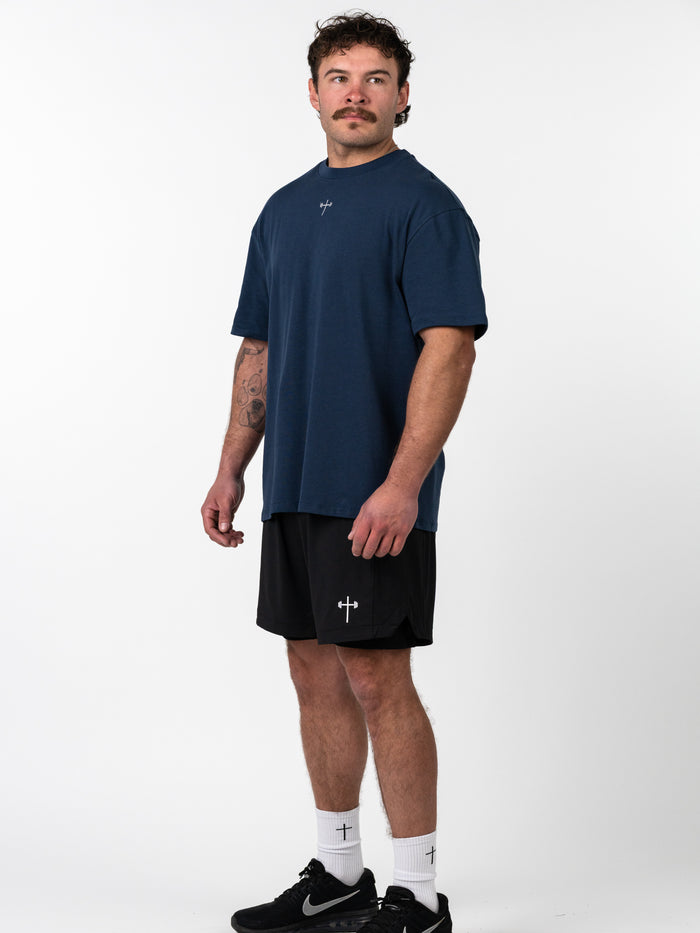 Man wearing a navy Classic Oversized Tee with a minimal cross design, paired with black shorts and white socks featuring Christian fitness apparel accents.
