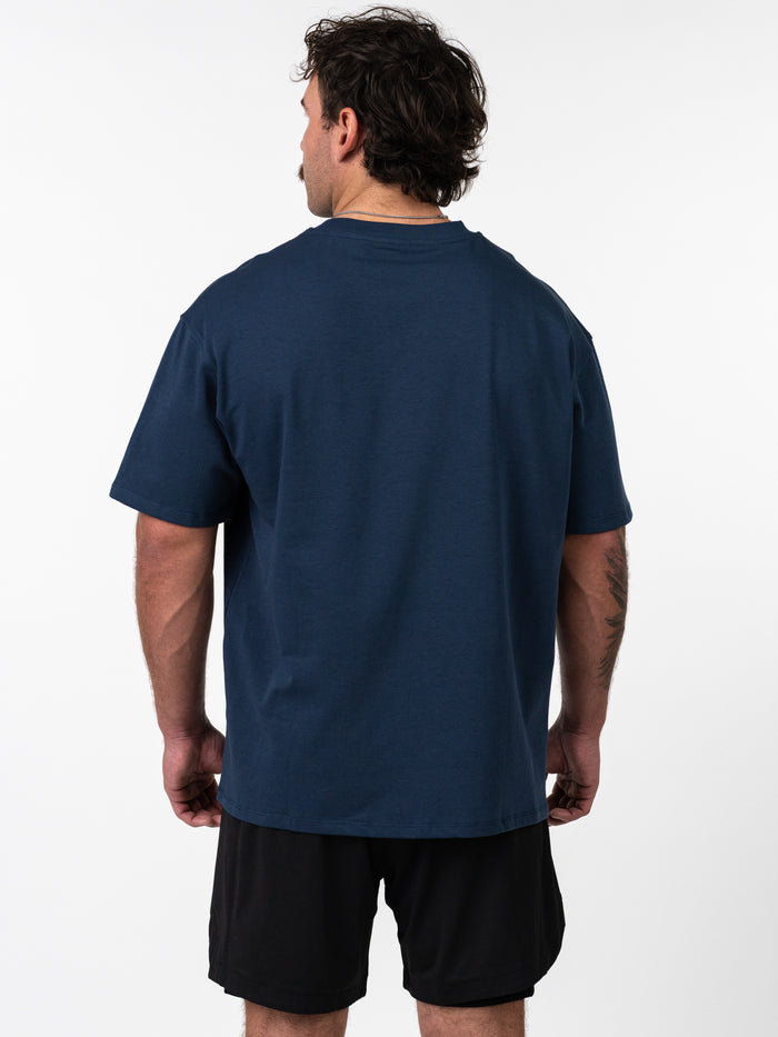 Man wearing a navy Classic Oversized Tee from the back, paired with black athletic shorts, showcasing the relaxed fit and structured fabric of the shirt.