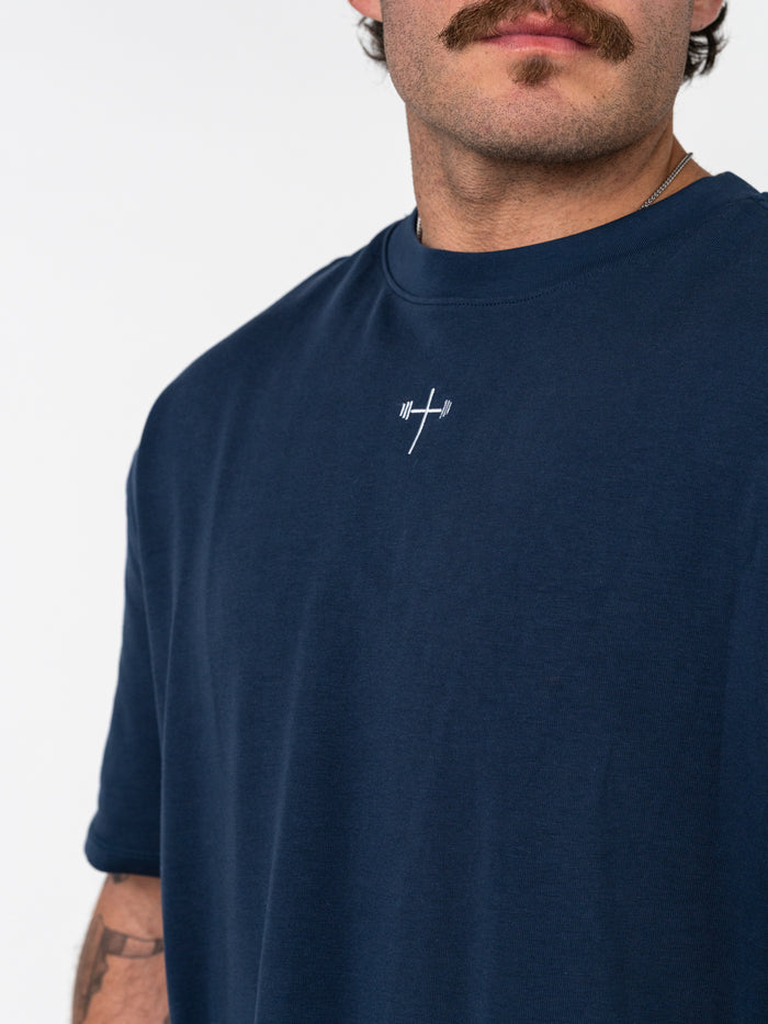 Close-up of a man wearing a navy blue Classic Oversized Tee featuring a small white barbell cross logo on the chest, combining faith and fitness in Christian gym clothing.
