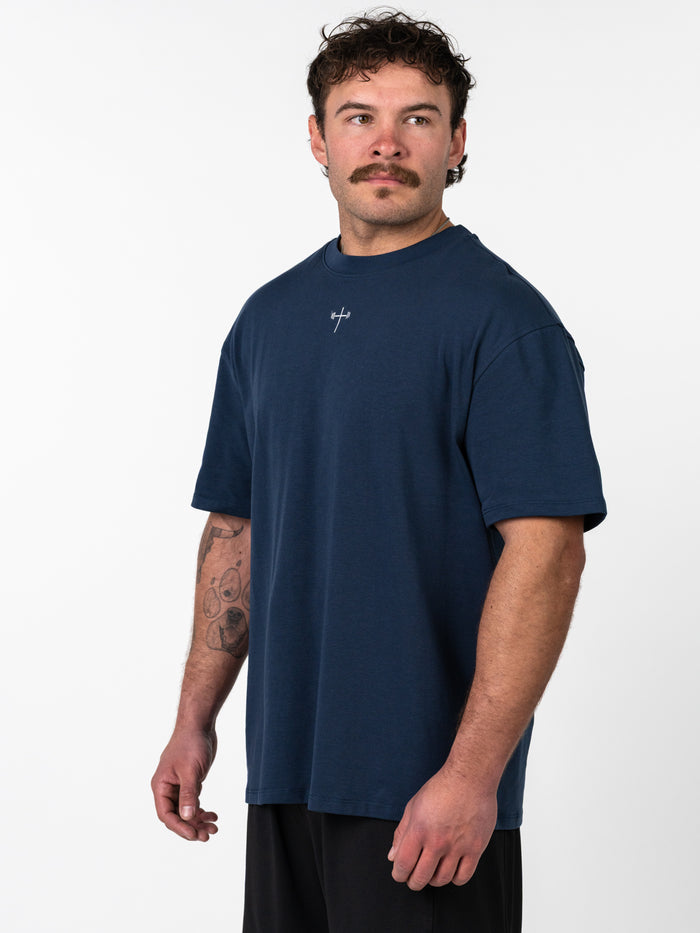 Man wearing a navy Classic Oversized Tee with a small cross and barbell design on the chest, styled for a relaxed, structured fit suitable for Christian fitness apparel.