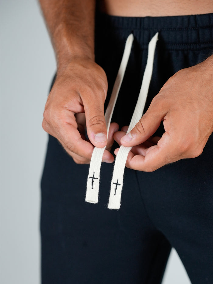 Person holding two white drawstrings with crosses on a plain background