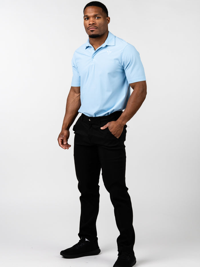 Man wearing a light blue Core Athletic Polo paired with black pants and black sneakers, standing against a plain white background in a confident pose.
