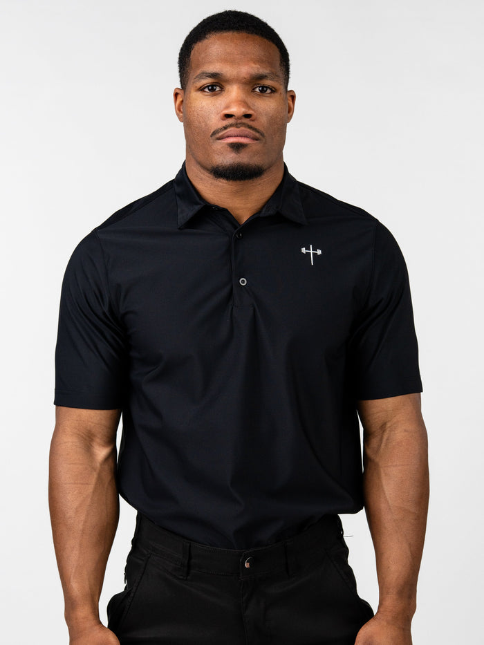 Male model wearing a black Core Athletic Polo with a subtle Christian cross and barbell logo on the chest, styled with black pants against a plain background.