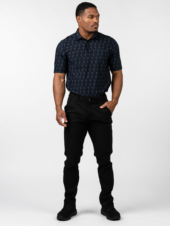 Man wearing a black Cross Premium Polo shirt with an all-over subtle cross pattern, paired with black pants and black shoes, posing against a white background.