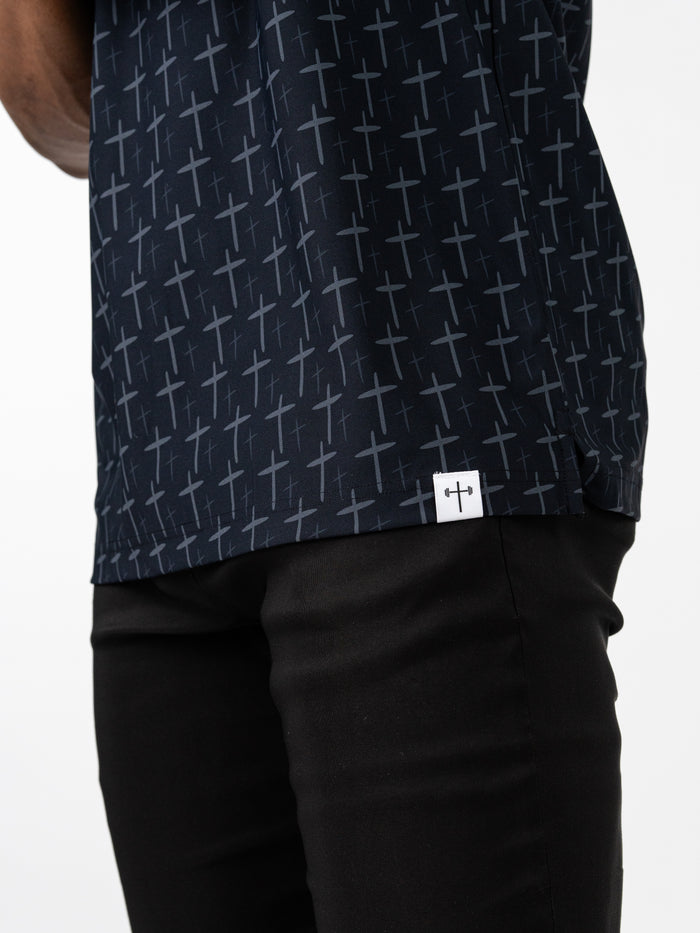 Close-up of a person wearing the Cross Premium Polo featuring an all-over subtle cross pattern on dark fabric, paired with black pants, highlighting Christian fitness apparel.