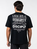 Man wearing a black Disciple Premium Oversized Tee with multiple stylized white "Disciple" text prints and a scripture reference Exodus 9:16 on the back, featuring Christian fitness apparel design.