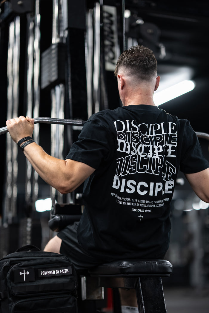 Man wearing Disciple Premium Oversized Tee performing a seated pull-down exercise in a gym, highlighting Christian fitness apparel with bold faith-based design.