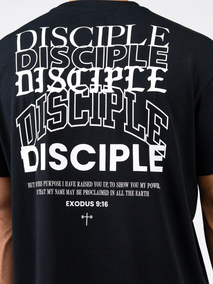 Back of black Disciple Premium Oversized Tee featuring multiple stylized white "DISCIPLE" text overlays, a biblical quote from Exodus 9:16, and a small cross with a barbell graphic.