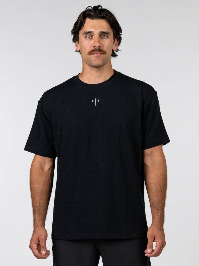 Man wearing a black t-shirt with a small white logo on a plain background