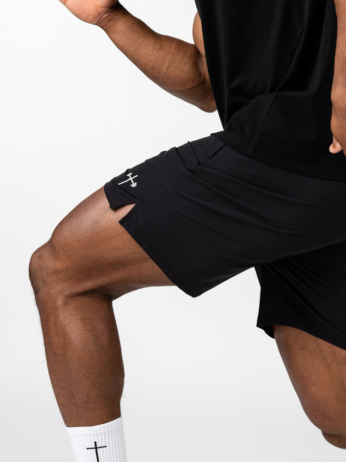 Athlete wearing black Essential Training Shorts featuring a subtle cross and barbell design, paired with white socks with a cross emblem, highlighting faith-based fitness apparel.
