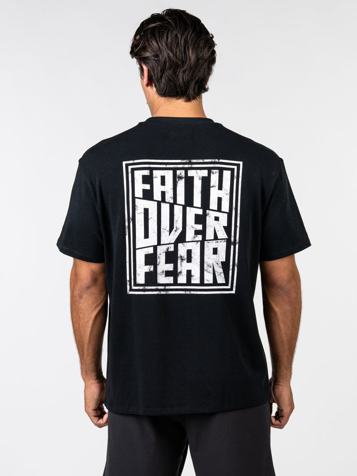 Man wearing black Faith Over Fear Premium Oversized Tee with bold white graphic text on back in a relaxed fit, styled for Christian fitness apparel and activewear.