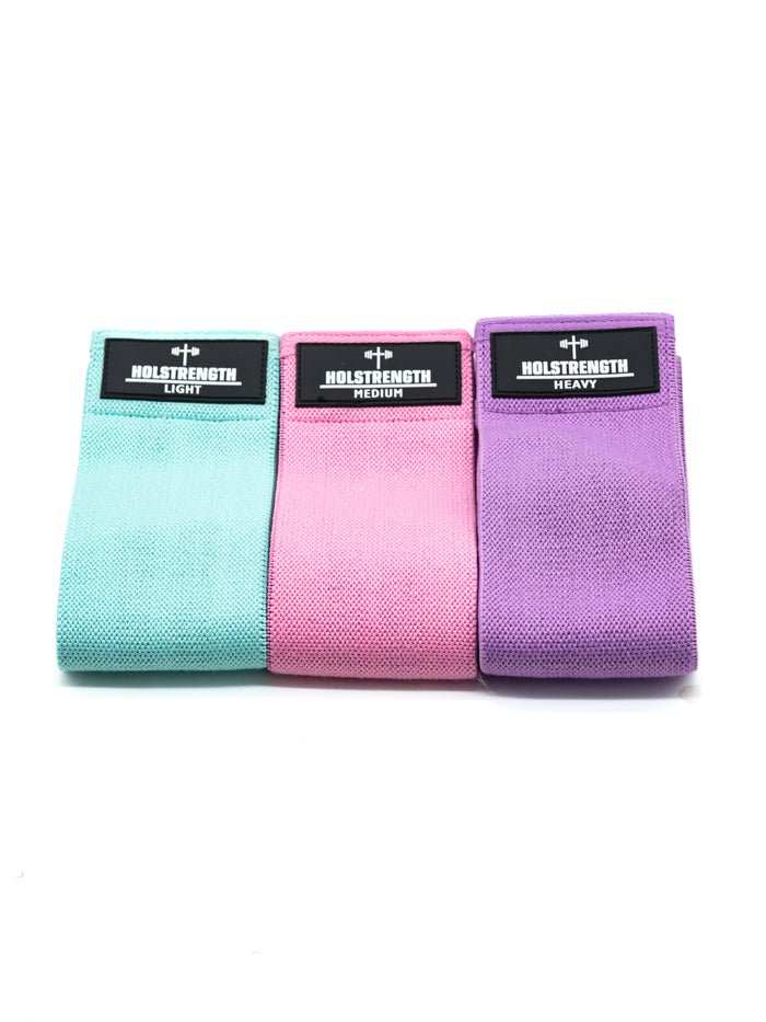 Set of three Glute Resistance Bands in light blue, pink, and purple with HolStrength branding, designed for home workouts to activate and strengthen hips and glutes.
