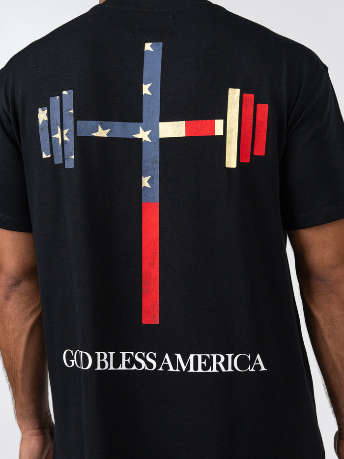 Back of God Bless America Premium Oversized Tee with a stylized barbell graphic featuring stars and stripes in red, white, and blue, and bold text reading God Bless America.