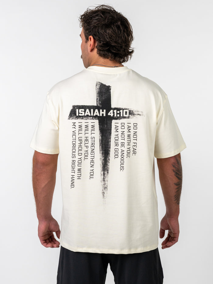 Man wearing the Isaiah 41:10 Premium Oversized Tee in cream color with a large black cross graphic and scripture text on the back, paired with black shorts, showcasing Christian fitness apparel.