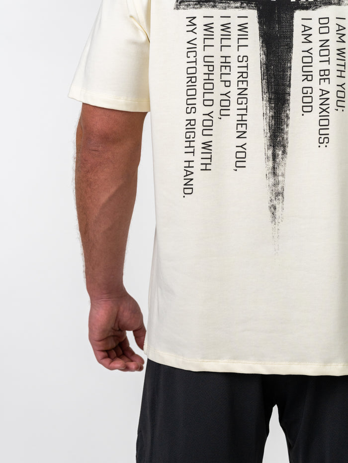 Person wearing a cream-colored Isaiah 41:10 Premium Oversized Tee featuring a large black cross and scripture text, paired with black shorts, shown from the back.