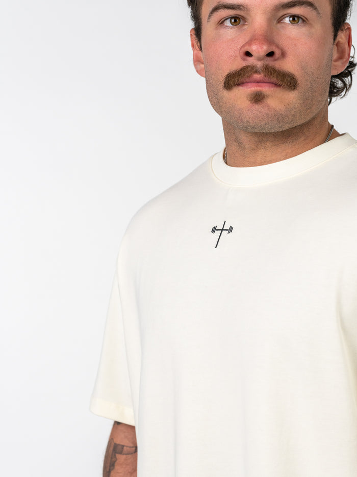 Man wearing a white Isaiah 41:10 Premium Oversized Tee featuring a small black graphic of a cross with a barbell in the center, representing Christian fitness apparel.