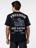Man wearing a black One Nation Under God Oversized Tee featuring a distressed American flag design and the words "FREEDOM ONE NATION Under God" on the back, paired with black shorts.