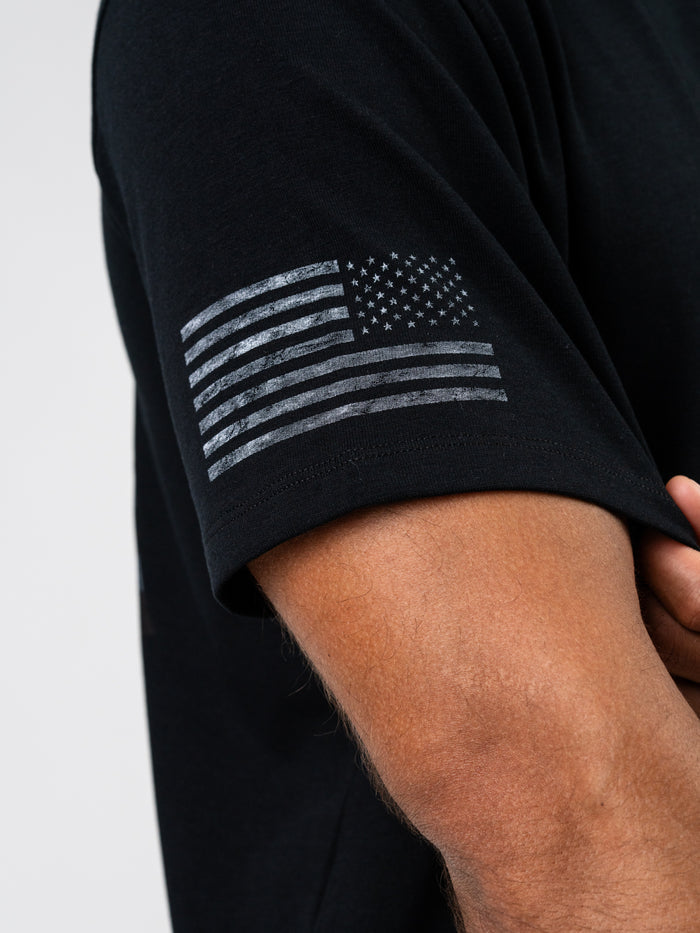 Close-up of a person wearing the One Nation Under God Oversized Tee, featuring a distressed grayscale American flag printed on the sleeve, highlighting its premium fabric and durable design.