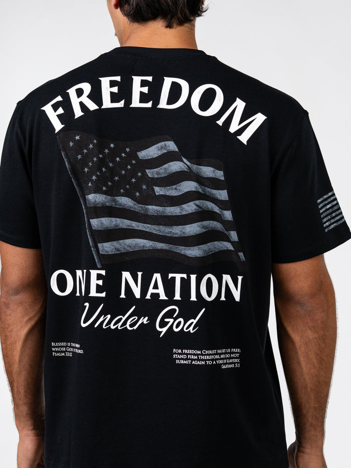 Back view of a person wearing the One Nation Under God Oversized Tee in black with a distressed American flag and bold white text emphasizing freedom and faith.