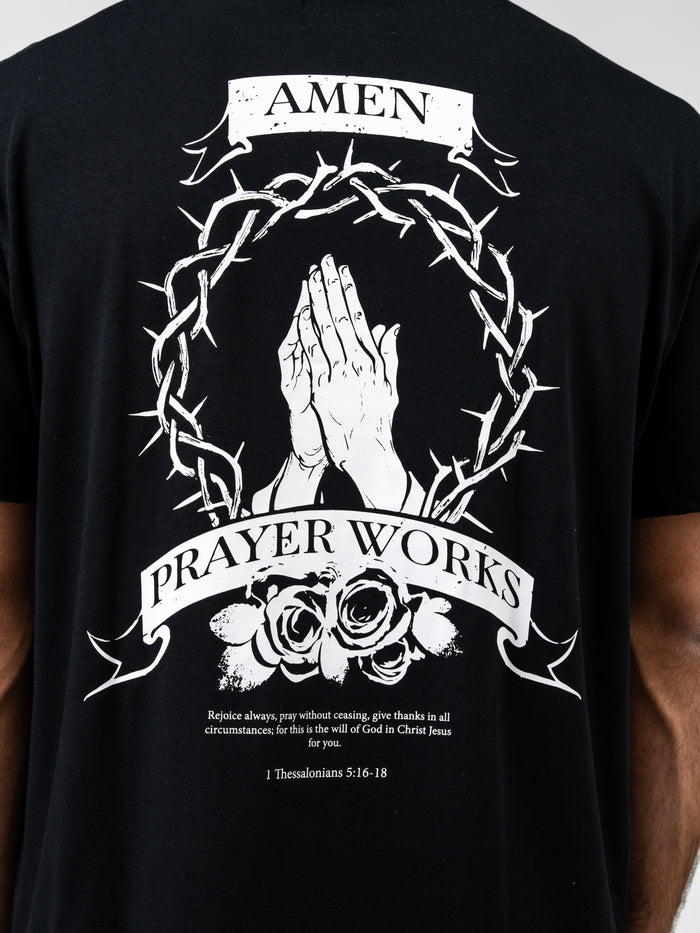 Back view of Prayer Works Premium Oversized Tee featuring white graphic of praying hands surrounded by a crown of thorns and roses, with text "Amen" and "Prayer Works" on black fabric.