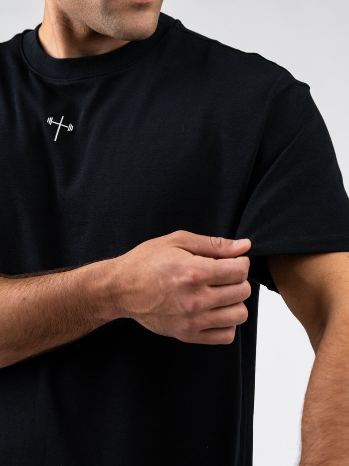 Close-up of a man wearing a black Prayer Works Premium Oversized Tee featuring a small white cross with a barbell design on the chest, representing Christian fitness apparel.