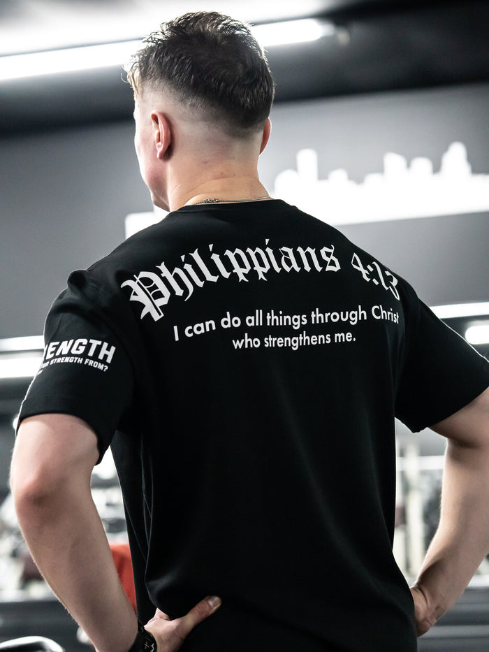 Person wearing a black t-shirt with 'Philippians 4:13' text, standing in an indoor setting.