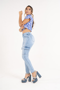 Woman wearing a blue patterned top and light blue jeans on a white background
