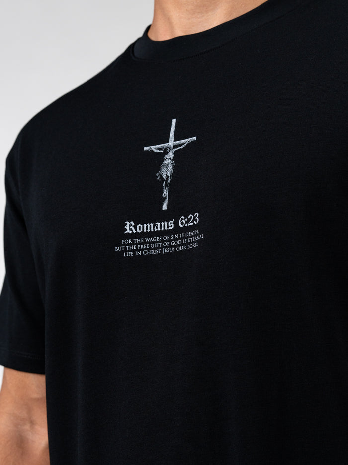 Close-up of a black Romans 6:23 “Wages of Sin” Premium Oversized Tee featuring a white crucifix design and biblical text in a structured, heavyweight fabric.