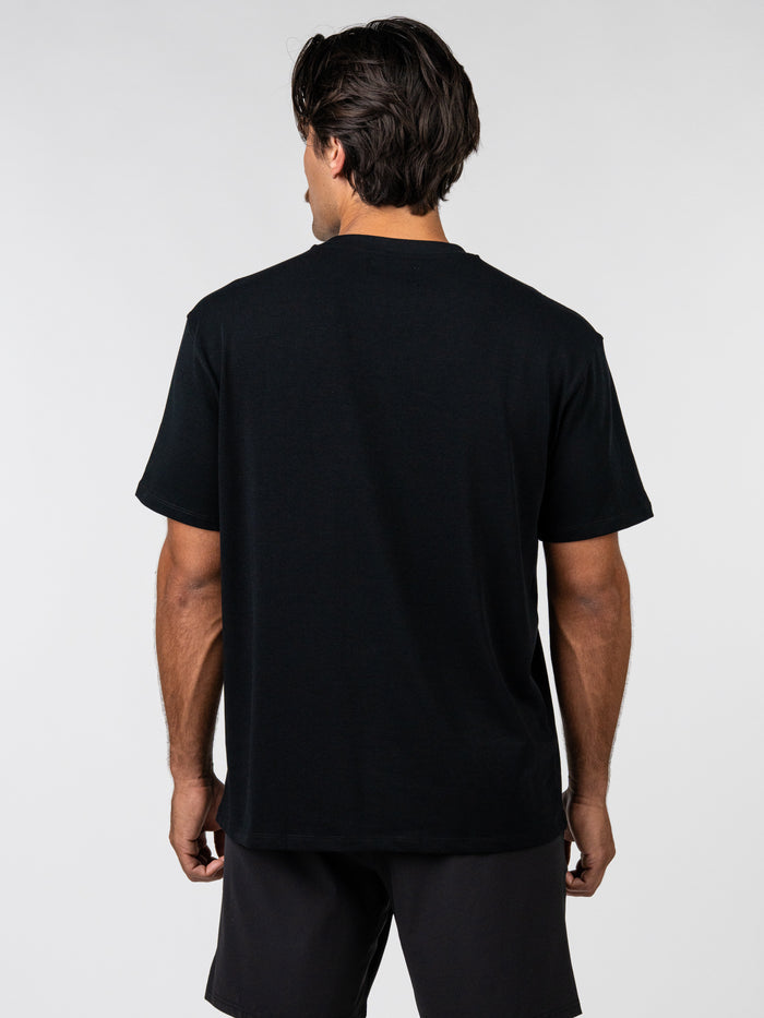 Rear view of a man wearing a black Romans 6:23 “Wages of Sin” Premium Oversized Tee, showcasing its relaxed fit and heavyweight fabric, styled with black shorts.