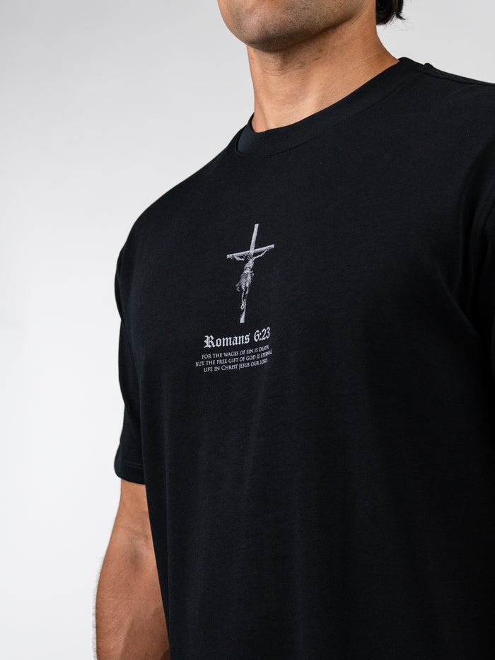 Man wearing a black Romans 6:23 “Wages of Sin” Premium Oversized Tee featuring a cross and scripture text, designed as Christian fitness apparel with a relaxed fit.