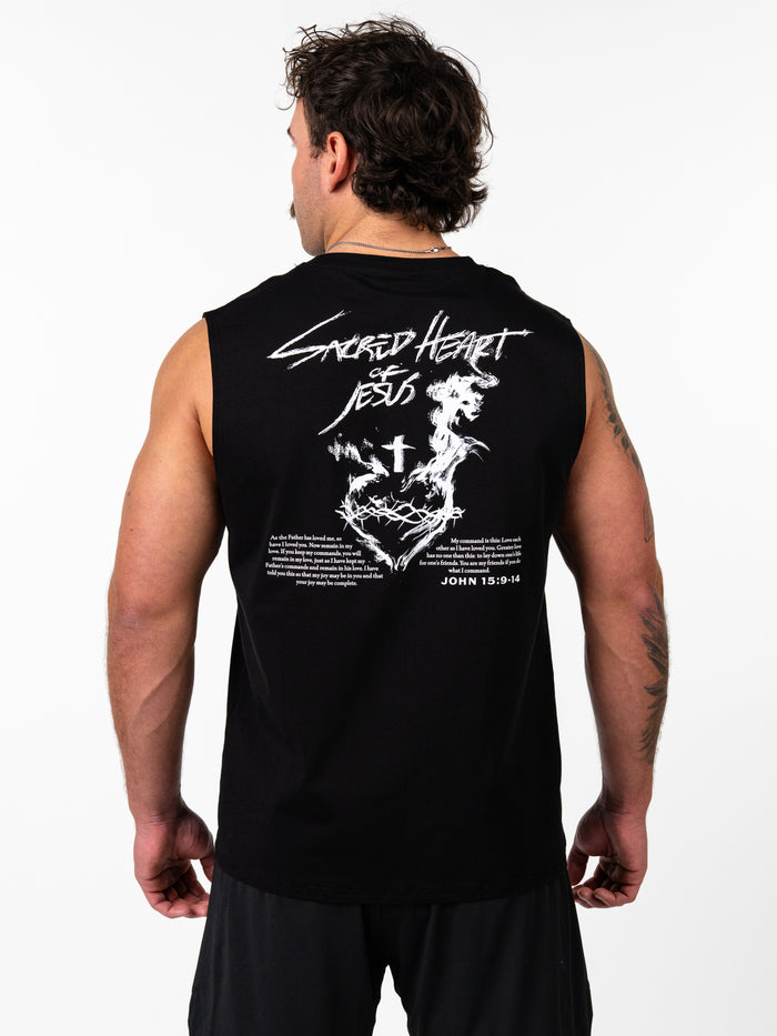 Man wearing a black Sacred Heart Premium Sleeveless Tank showing the back design featuring a stylized sacred heart with a cross, crown of thorns, and scripture text from John 15:9-14, representing Christian fitness apparel.