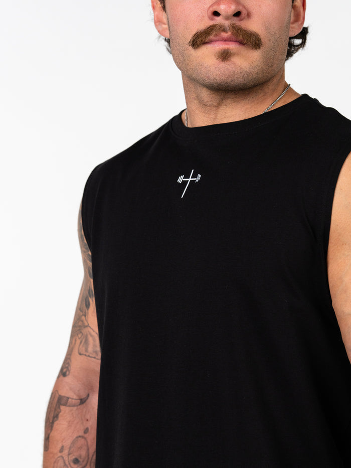 Man wearing a black Sacred Heart Premium Sleeveless Tank featuring a small white Christian cross with a barbell design on the chest, showcasing Christian fitness apparel.