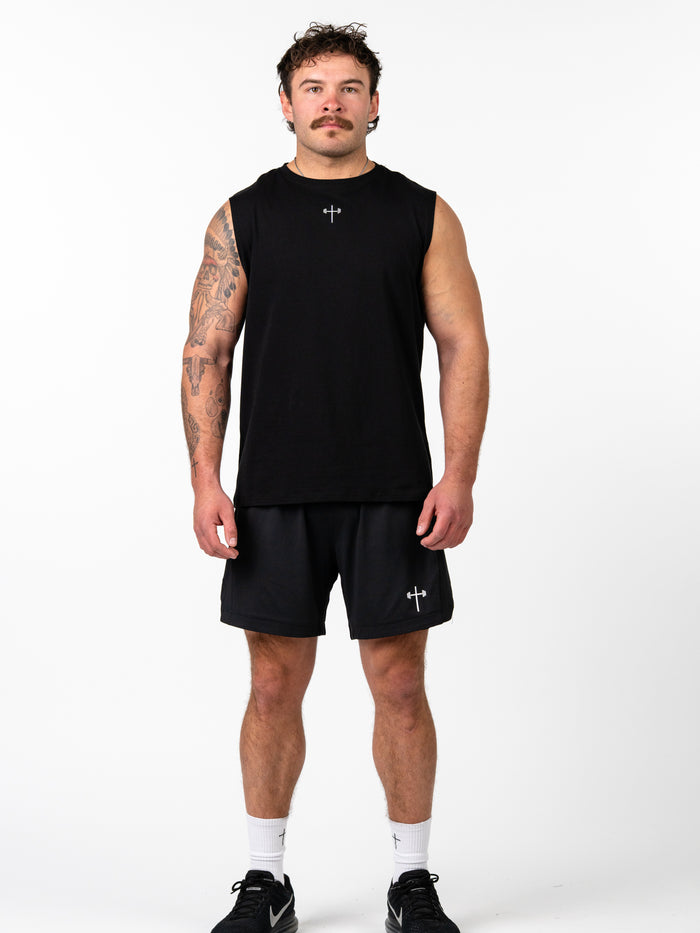 Man wearing Sacred Heart Premium Sleeveless Tank in black with a small Christian cross and barbell design, paired with matching black shorts and athletic shoes.