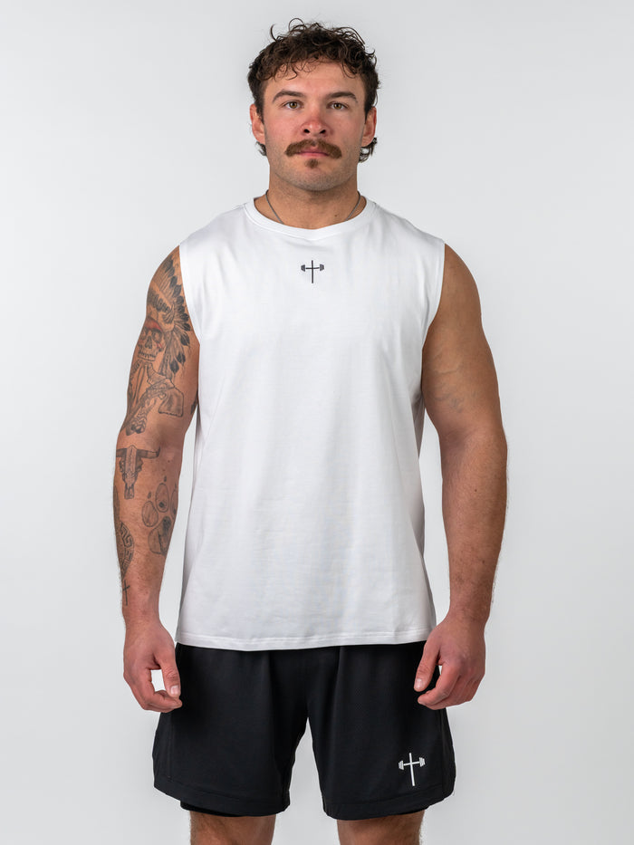 Man wearing a white Sacred Heart Premium Sleeveless Tank with a small black cross and barbell design on the chest, paired with black shorts featuring a matching symbol.