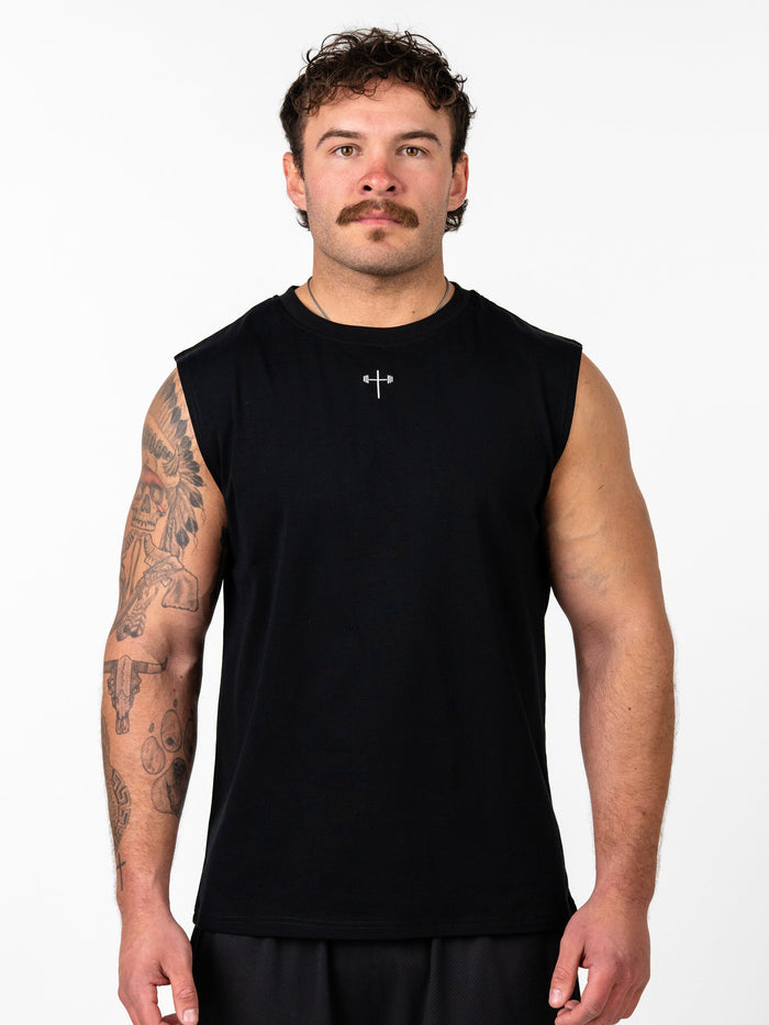Man wearing a black Scripture Premium Sleeveless Tank featuring a small cross and barbell design at the chest, styled for Christian fitness apparel.