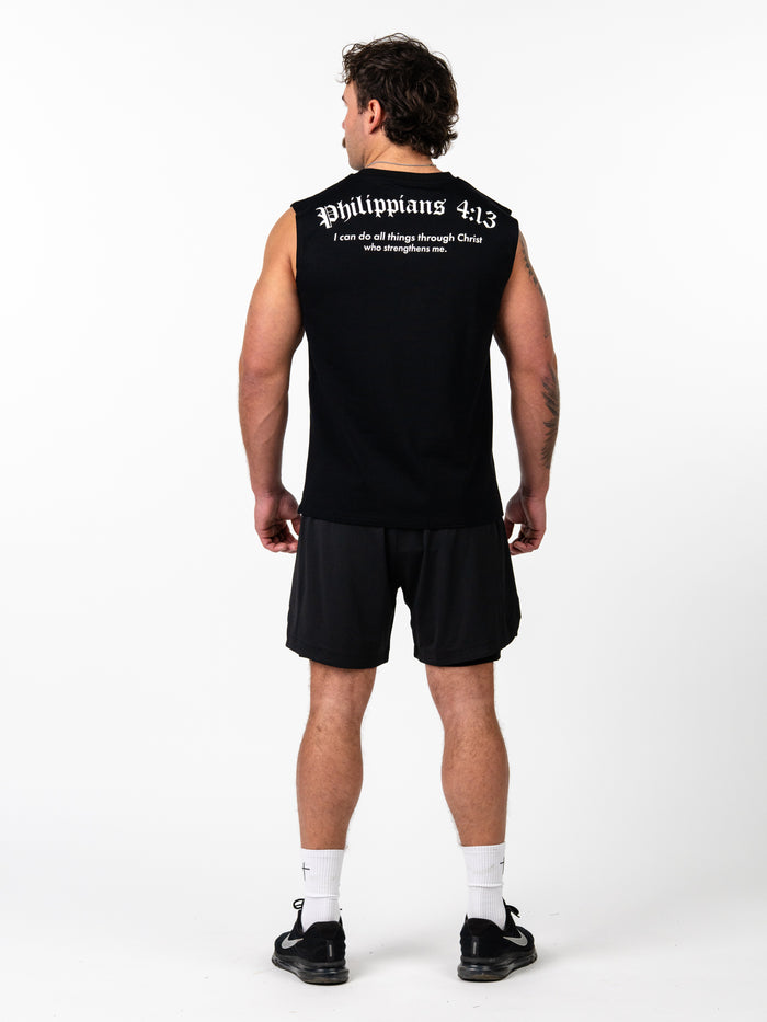 Male model seen from behind wearing a black Scripture Premium Sleeveless Tank with Philippians 4:13 scripture text, paired with black shorts, white socks, and black athletic shoes.