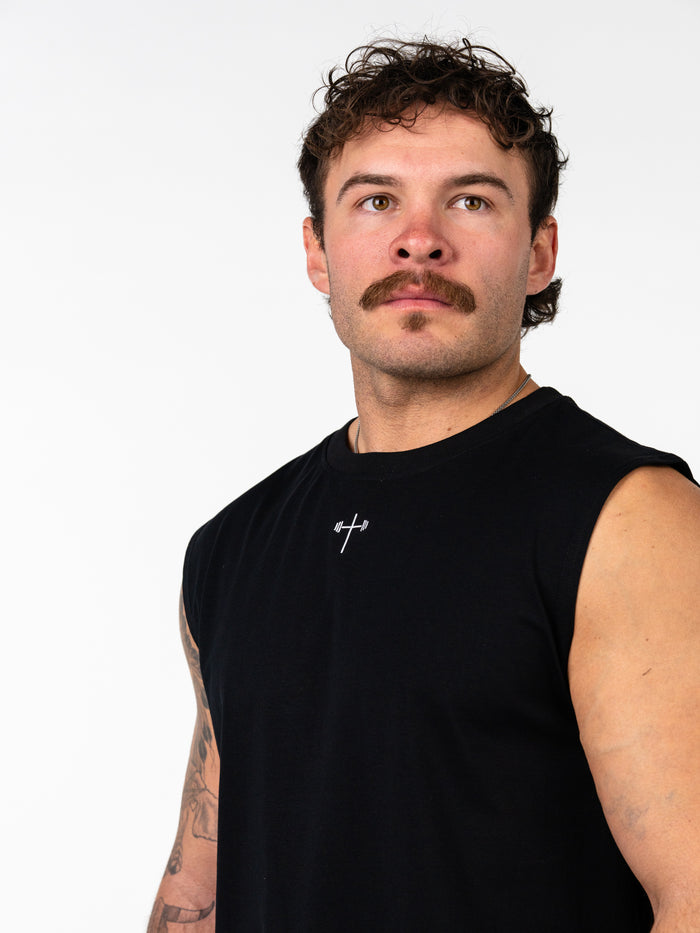 Man wearing a black Scripture Premium Sleeveless Tank with a small white cross and barbell logo on the chest, showcasing Christian fitness apparel.