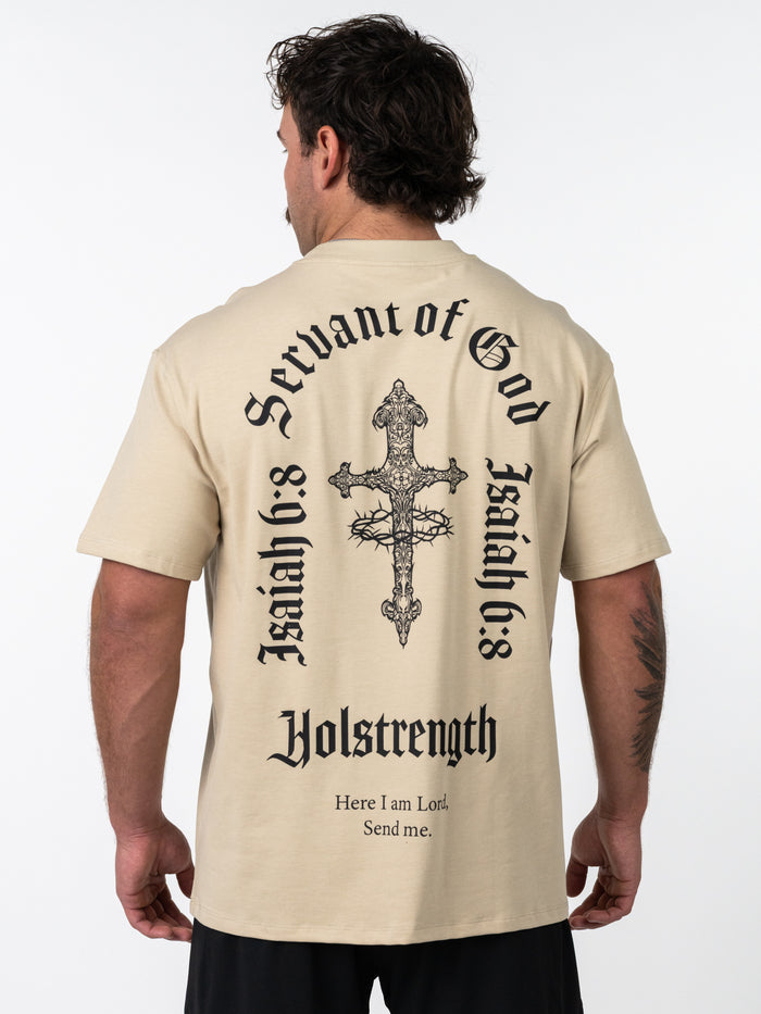 Man wearing a beige Servant of God Premium Oversized Tee with a detailed black cross and crown of thorns graphic on the back, accompanied by text referencing Isaiah 6:8 and Holstrength, showcasing Christian fitness apparel.