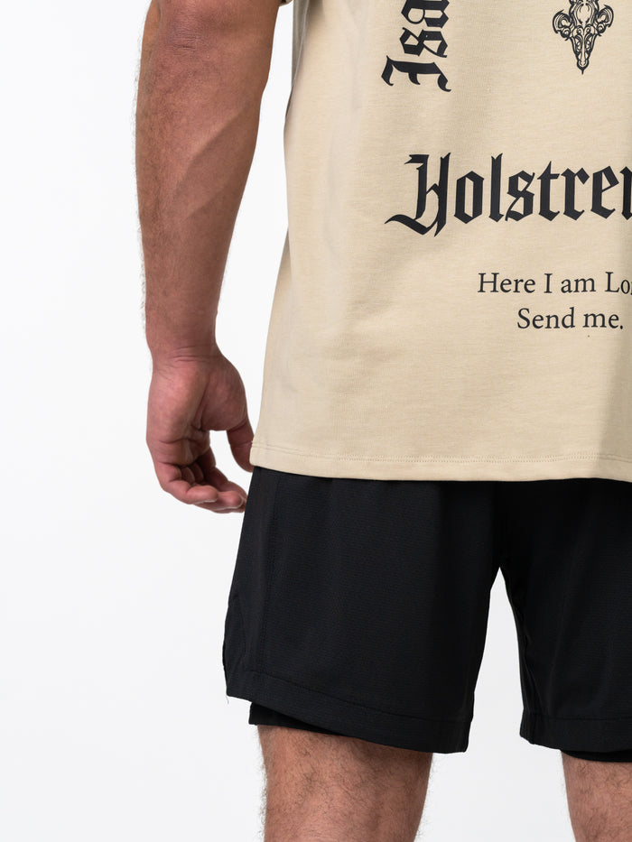 Close-up of a person wearing the Servant of God Premium Oversized Tee in beige with black text and design, paired with black athletic shorts, showcasing Christian fitness apparel.